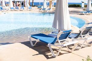 Swimming pool with clean clear water, nobody. Square shaped pool with blue tiles with grab bars ladder and sunbeds on the decks, no people. water surface. Overhead view. Summer background. photo