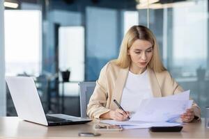 Focused professional reviewing documents at her desk in a contemporary office setting, displaying efficiency and concentration. photo
