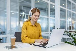 Smiling woman programmer working remotely with laptop and headphones in a modern office. Concept of remote work, technology, and professional development. photo