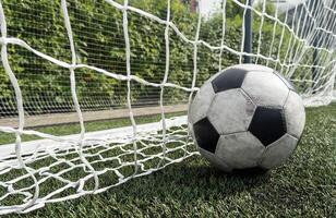 Soccer football in Goal net with green grass field. photo