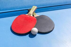 Two table tennis or ping pong rackets and ball on blue table with net photo