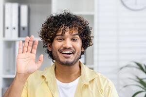Smiling young man waving during a call. Friendly and happy interaction in a home office setting. photo