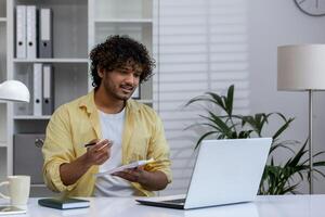 Young man taking notes while engaging in an online course. Learning remotely at home with a laptop in a modern workspace. photo