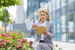 Businesswoman in a suit reading an envelope with a surprised expression outside an office building. Concept of unexpected news and concern. photo