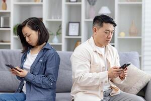 Couple sitting apart on a sofa, focusing on their smartphones. Concept of technology affecting relationships and communication. photo
