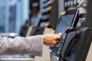 Closeup of a person's hand swiping a credit card at a payment terminal in a retail store for a transaction. photo