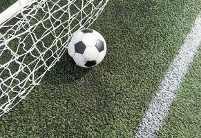 Soccer football in Goal net with green grass field. photo