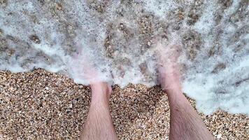 Bare feet in foamy ocean waves on a pebbled beach, representing a relaxing summer vacation or seaside getaway video