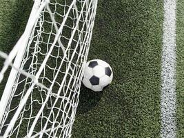 Soccer football in Goal net with green grass field. photo