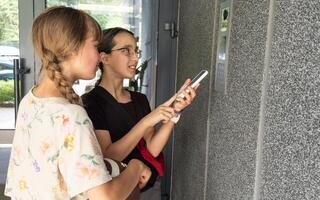 two teenagers getting access to the building by attaching smartphone to intercom. Concept of modern security technologies for access and smart home photo