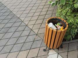 A garbage bin with a garbage bag is installed in a public place, a park. Located close to sidewalk. photo