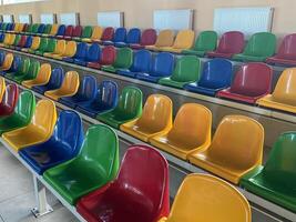 Multicolored Empty plastic chairs in the stands of the stadium. Many empty seats for spectators in the stands. Empty plastic chairs for football fans in the gym. Bright colorful seats for stadium fans photo