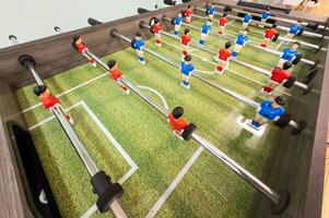 Classic Foosball Table Game With Players in Red and Blue Jerseys During Daytime Indoor Match. Close-up view of foosball table featuring red and blue jersey players positioned for daytime indoor game. photo