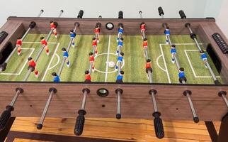 Classic Foosball Table Game With Players in Red and Blue Jerseys During Daytime Indoor Match. Close-up view of foosball table featuring red and blue jersey players positioned for daytime indoor game. photo