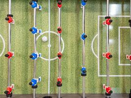 Classic Foosball Table Game With Players in Red and Blue Jerseys During Daytime Indoor Match. Close-up view of foosball table featuring red and blue jersey players positioned for daytime indoor game. photo