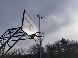A basketball net under a cloudy sky. The back board has been busted and is now covered with a large piece of wood. photo