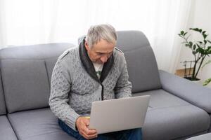 Older man sitting on sofa, smiling at computer screen at home photo