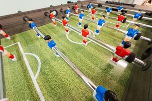 Classic Foosball Table Game With Players in Red and Blue Jerseys During Daytime Indoor Match. Close-up view of foosball table featuring red and blue jersey players positioned for daytime indoor game. photo