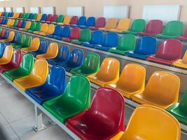 Multicolored Empty plastic chairs in the stands of the stadium. Many empty seats for spectators in the stands. Empty plastic chairs for football fans in the gym. Bright colorful seats for stadium fans photo