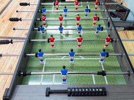 Classic Foosball Table Game With Players in Red and Blue Jerseys During Daytime Indoor Match. Close-up view of foosball table featuring red and blue jersey players positioned for daytime indoor game. photo