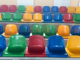 Multicolored Empty plastic chairs in the stands of the stadium. Many empty seats for spectators in the stands. Empty plastic chairs for football fans in the gym. Bright colorful seats for stadium fans photo