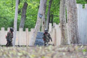 Paintball game. Players with weapons shooting paint balls. Men on the playground. Guys in camouflage and masks are fighting. photo