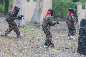 Paintball game. Players with weapons shooting paint balls. Men on the playground. Guys in camouflage and masks are fighting. photo