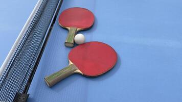 Two table tennis rackets and balls on a blue table with net. photo