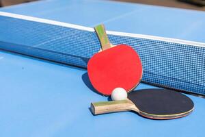 Two table tennis or ping pong rackets and ball on blue table with net photo