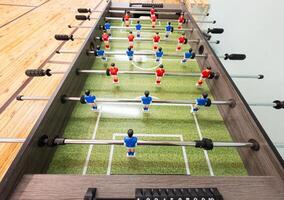Classic Foosball Table Game With Players in Red and Blue Jerseys During Daytime Indoor Match. Close-up view of foosball table featuring red and blue jersey players positioned for daytime indoor game. photo