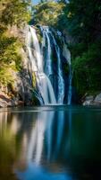 Rushing waterfall with sunlit glow, reflective pool, vibrant greenery in peaceful setting Vertical Mobile Wallpaper photo
