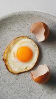 Fried egg on speckled surface with intact yolk, broken shell, simple backdrop Vertical Mobile Wallpaper photo