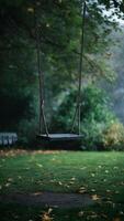 Empty swing in serene park, surrounded by lush greenery and fallen leaves Vertical Mobile Wallpaper photo