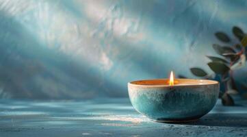 A Single Candle Burning on a Blue Tabletop With Greenery in the Background photo