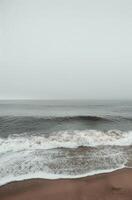 Grey Skies and Foamy Waves on a Sandy Beach photo
