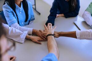 A group of doctors and a medical nurse join their hands together on a table, showcasing the unwavering teamwork and solidarity that drives their collective efforts in the healthcare field photo