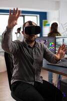 Videographer wearing VR headset and gesturing editing project in post production software sitting in studio office. Man maker employee processing film montage in digital multimedia company photo