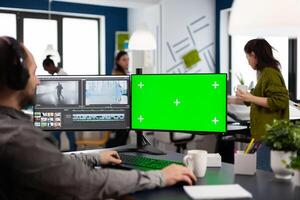 Videographer using computer with chroma key, mock up isolated display editing and audio footage. Man editor processing film montage on pc with green screen while team working in background photo