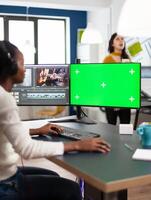 Black videographer using computer with chroma key, mock up isolated display editing and audio footage. Woman editor processing film montage on green screen working in digital multimedia company photo