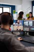 Videographer employee having conference wearing headset editing client movie, getting feedback on commercial project. Freelancer using post production software on pc in creative office. photo