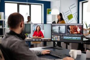 Videographer in web online conference with project manager on call editing client work, getting feedback on commercial movie using post production software on two monitors in start up office photo
