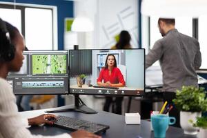 African woman editor with headset talking during online conference with partner on call editing client work, getting feedback on commercial movie using post production software on pc in office photo