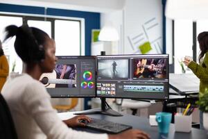 African editor working with footage and sound, editing new project cutting film montage sitting in modern agency office. Woman using computer processing movie in post production software photo