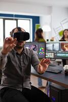 editor experiencing virtual reality goggles prosessing film montage in post production software sitting in creative workplace. Videographer with VR Glasses working in multimedia studio office. photo