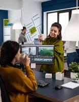 Team of videographers talking about project while drinking coffee working in editing app at pc sitting in digital multimedia company. Creative women having break while prosessing film montage photo