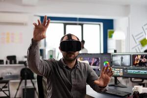 editor experiencing virtual reality headset, gesturing, editing film montage using post production software working in creative agency office. Videographer using VR goggles in multimedia company photo