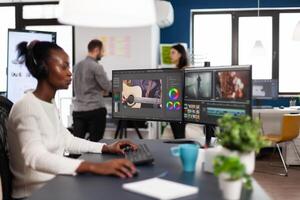 African videographer wearing headset editing movie using post production software working in creative start up agency office. Black editor processing footage on computer with dual displays photo