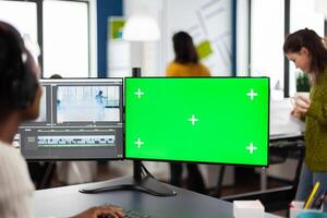 African woman videographer with headset processing film montage working at greenscreen, chroma key isolated display of computer. editor editing movie in post production software in agency office photo