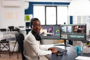 Black videographer smiling at camera editing project in post production software working in creative studio office. African movie maker editing audio film montage on professional computer photo