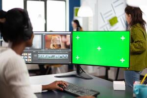 Black woman editor developing new project film montage looking at greenscreen, chroma key isolated display of computer, sitting in creative agency. Creator processing movie with modern software photo